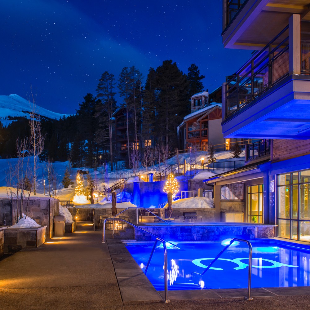 Outdoor pool at Grand Colorado on Peak 8 — lit at night, snow banked around it, evergreens and stars overhead.
