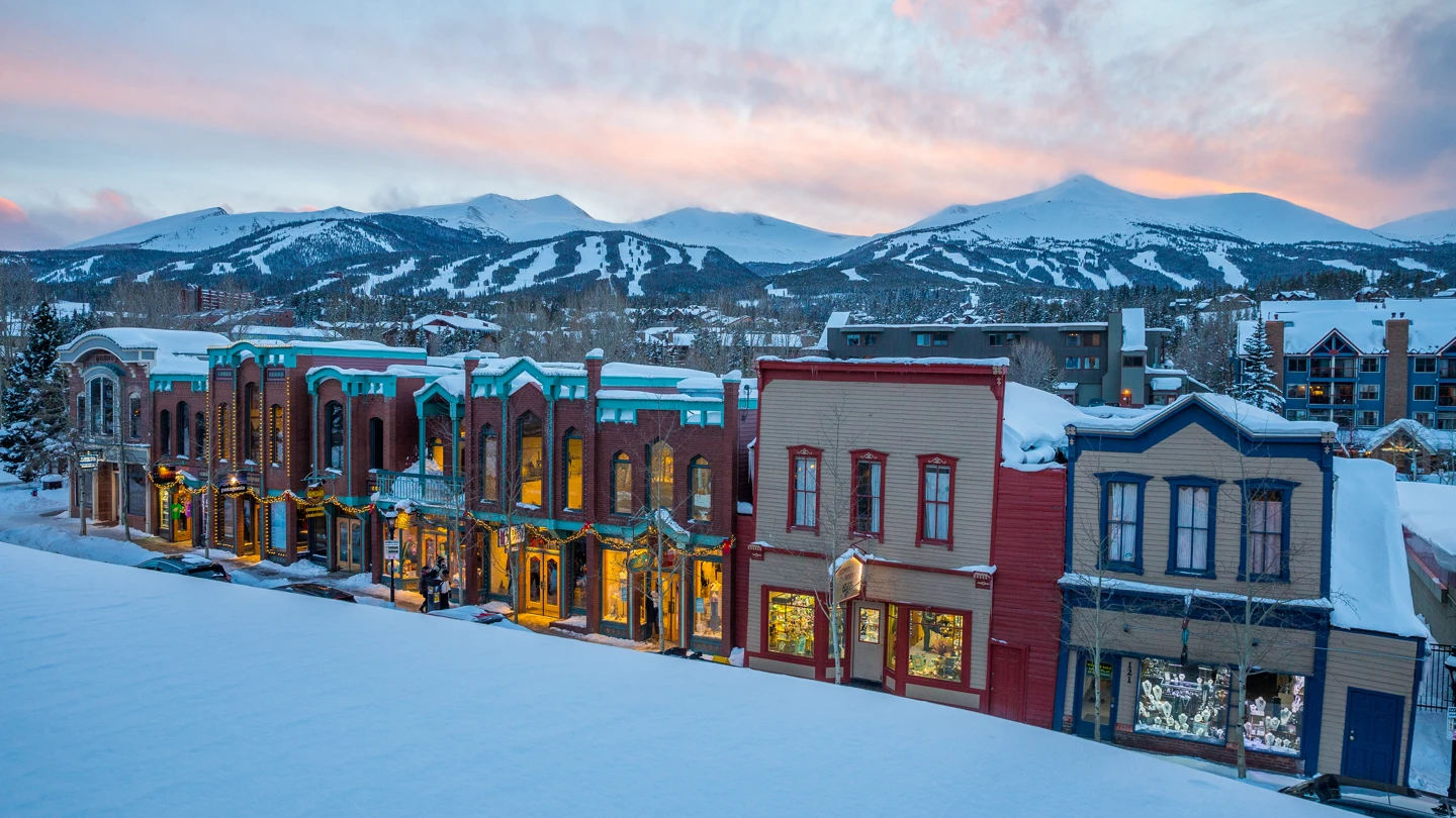 Downtown Breckenridge at dusk — historic Main Street shopfronts lit against the ski runs of Peak 8 behind them.