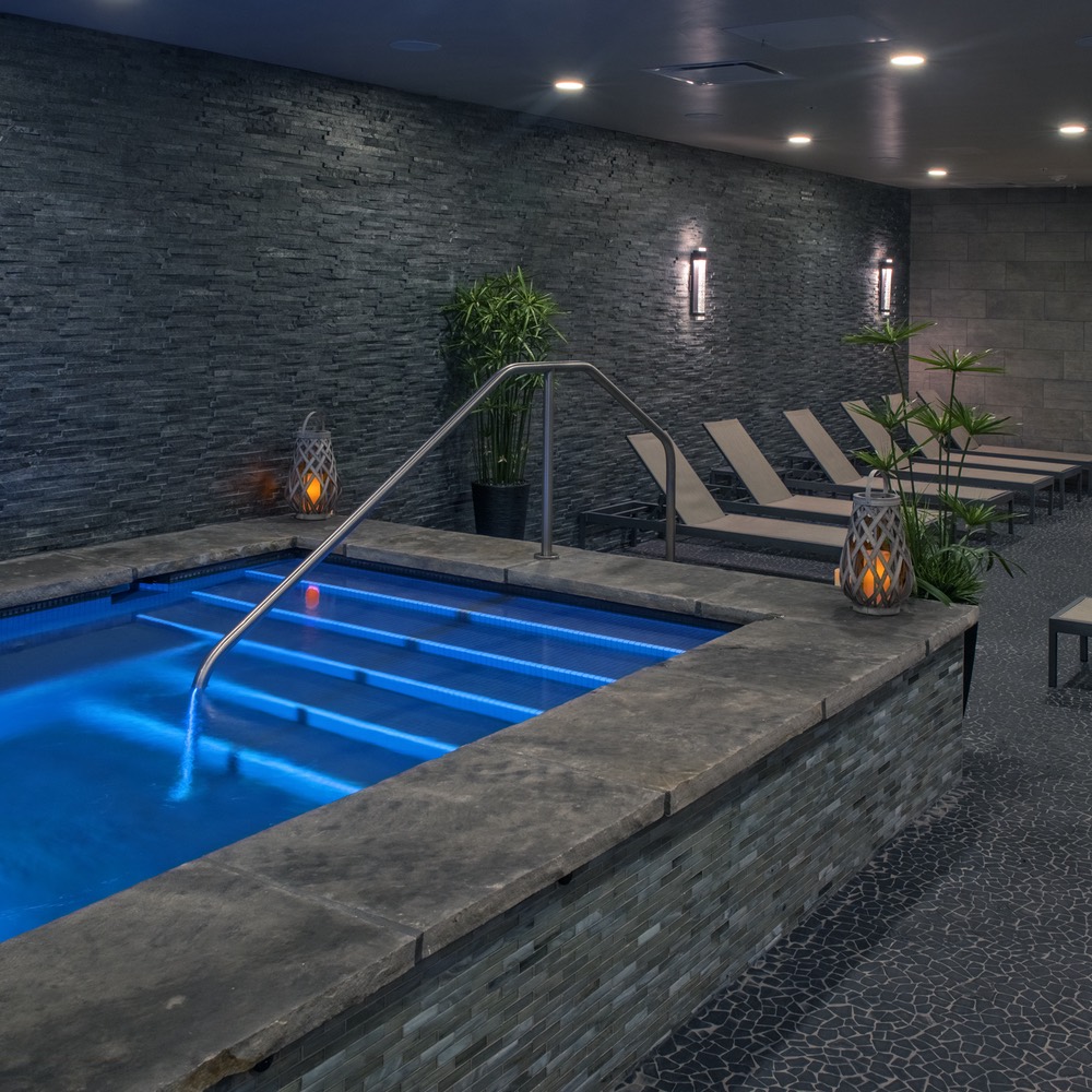 Indoor spa pool at Grand Colorado on Peak 8 — stacked stone wall, lantern light, chaise loungers beside a lap-length plunge pool.